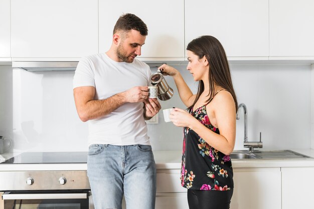 Mujer joven que vierte el café en la taza de su novio