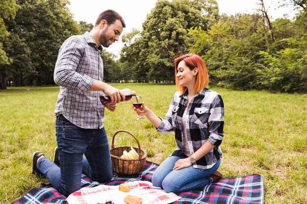 Una mujer joven que vierte el vino en el vaso de su esposa en un picnic en el parque