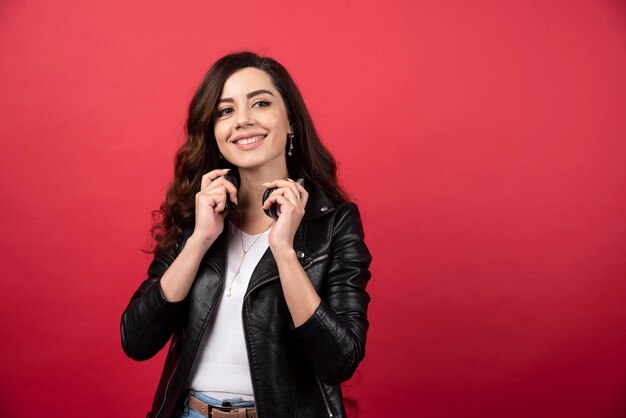 Mujer joven quitándose los auriculares y posando sobre un fondo rojo. Foto de alta calidad