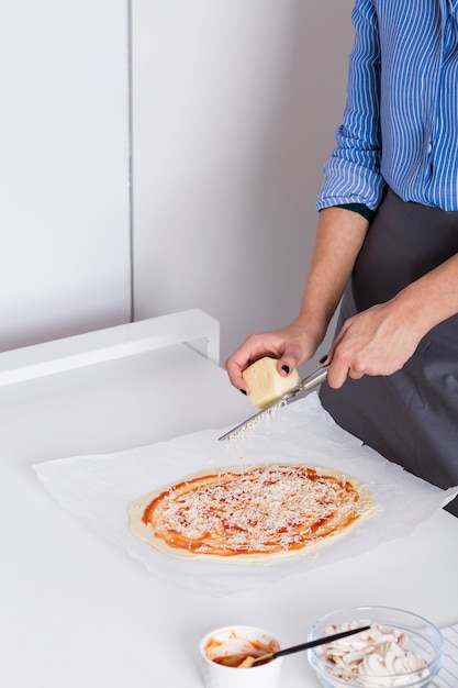 Mujer joven rallar el queso en pizza de masa casera