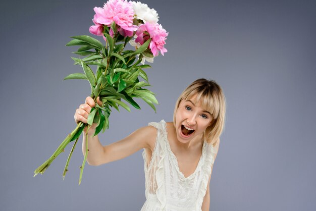 Foto gratuita mujer joven con ramo de flores sobre pared gris