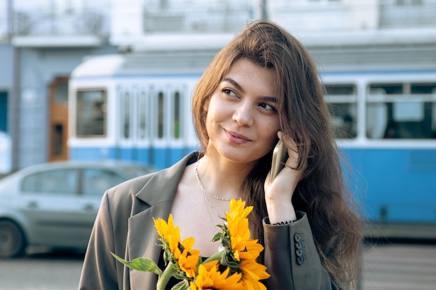 Una mujer joven con un ramo de girasoles está hablando por teléfono al atardecer