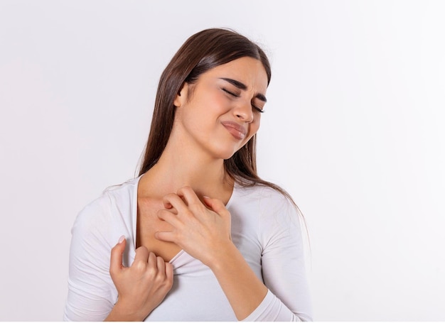 Mujer joven rascándose el cuello debido a la picazón en un fondo gris La mujer tiene picazón en el cuello El concepto de síntomas de alergia y atención médica