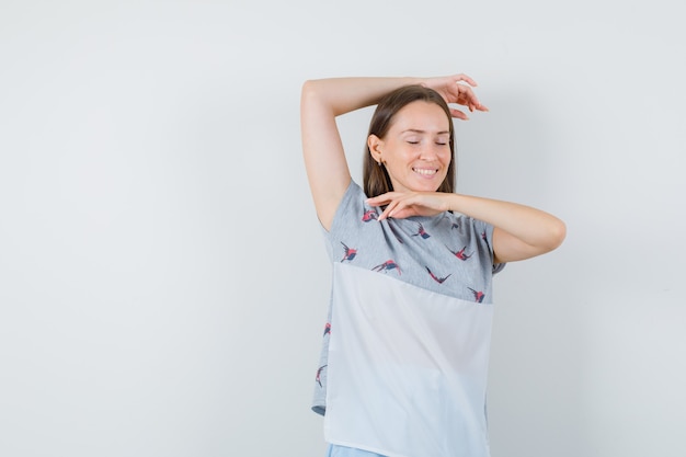 Mujer joven realizando gesto de baile en camiseta y mirando contento, vista frontal.