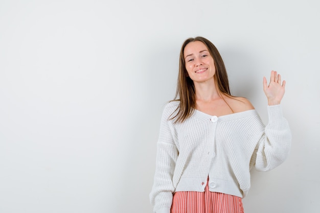 Foto gratuita mujer joven en rebeca y falda agitando la mano para saludar mirando feliz aislado