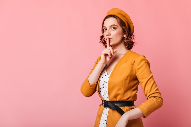 Mujer joven refinada en boina mostrando signo secreto. Modelo femenino bastante francés tocando los labios con el dedo.