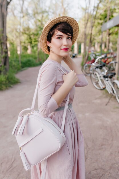 Mujer joven refinada con pelo corto y piel pálida posando en la calle, llevando una moderna mochila blanca