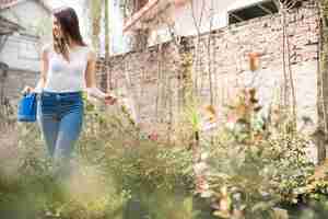 Foto gratuita mujer joven con regadera de pie entre las plantas en crecimiento