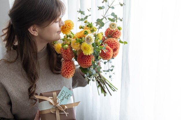 Mujer joven con un regalo para el día de la madre y un ramo de flores en sus manos