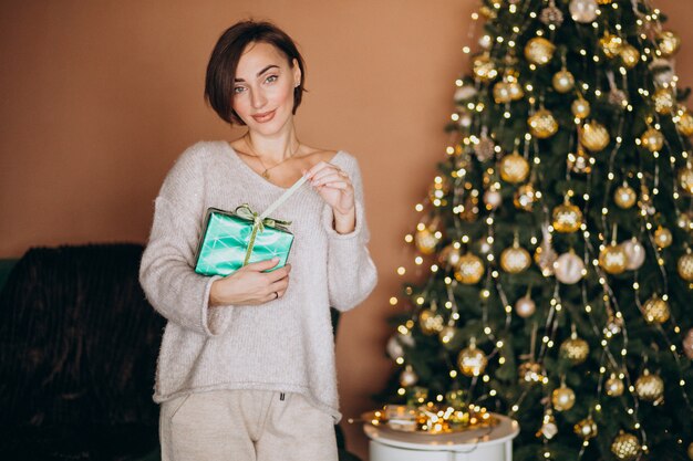 Mujer joven con regalo de Navidad junto al árbol de Navidad