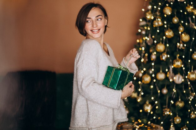 Foto gratuita mujer joven con regalo de navidad junto al árbol de navidad