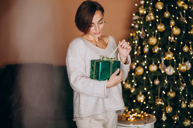 Mujer joven con regalo de Navidad junto al árbol de Navidad