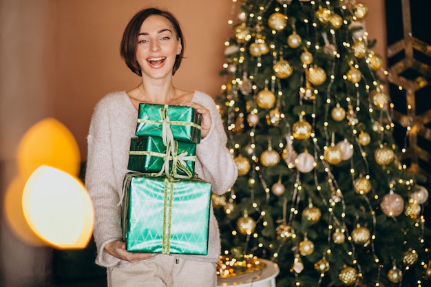 Mujer joven con regalo de Navidad junto al árbol de Navidad