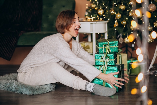 Mujer joven con regalo de Navidad junto al árbol de Navidad