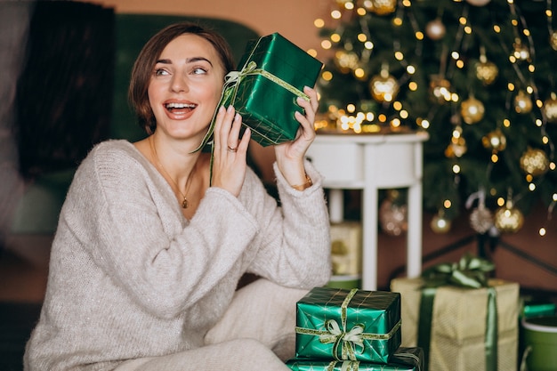 Mujer joven con regalo de Navidad junto al árbol de Navidad