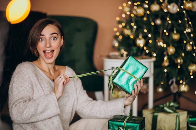 Mujer joven con regalo de Navidad junto al árbol de Navidad