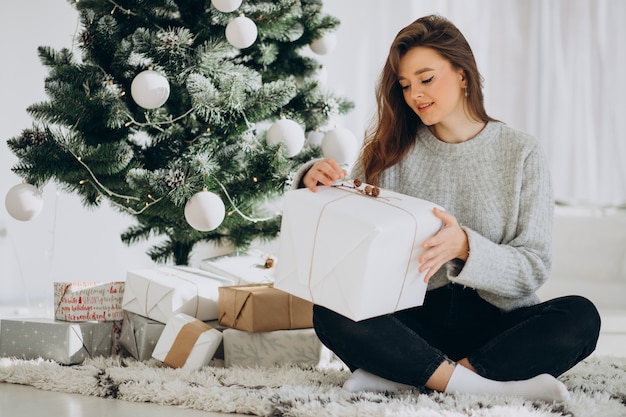 Mujer joven con regalos de navidad por el árbol de navidad