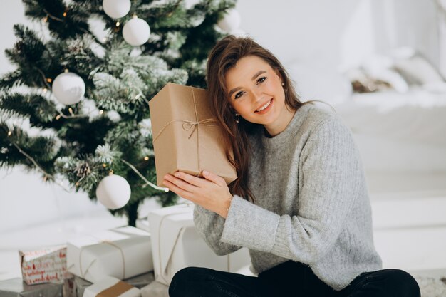 Mujer joven con regalos de navidad por el árbol de navidad