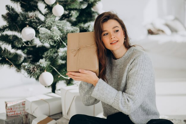 Mujer joven con regalos de navidad por el árbol de navidad