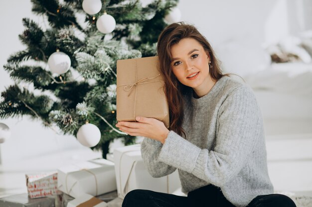 Mujer joven con regalos de navidad por el árbol de navidad