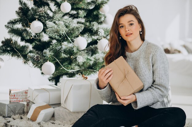 Mujer joven con regalos de navidad por el árbol de navidad