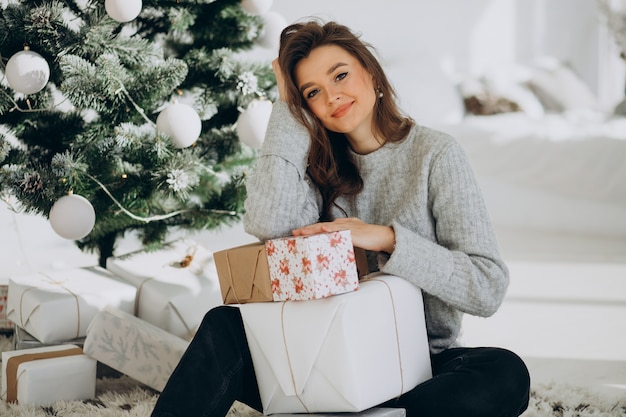 Mujer joven con regalos de navidad por el árbol de navidad