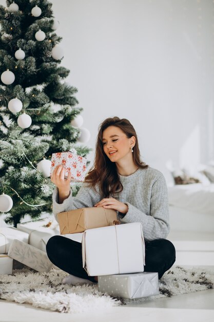 Mujer joven con regalos de navidad por el árbol de navidad