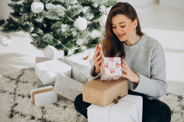 Mujer joven con regalos de navidad por el árbol de navidad