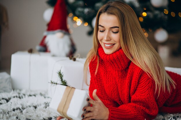 Mujer joven con regalos de navidad por el árbol de navidad