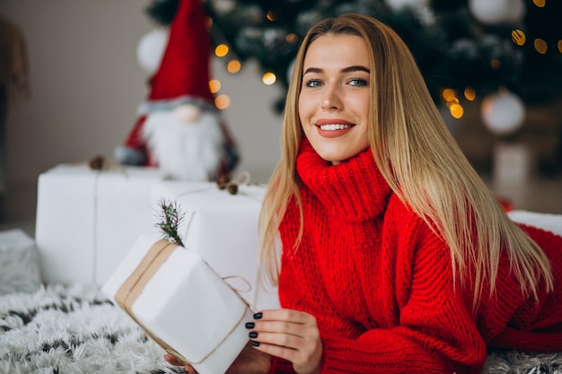 Mujer joven con regalos de navidad por el árbol de navidad