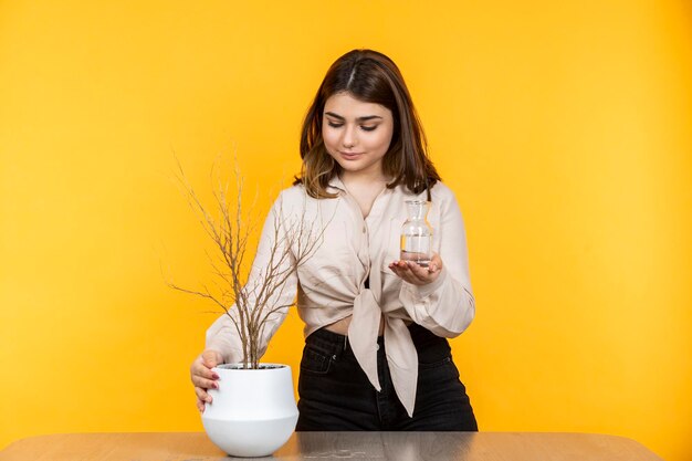 Mujer joven regando plantas secas Hermosa chica de pie sobre fondo amarillo Foto de alta calidad