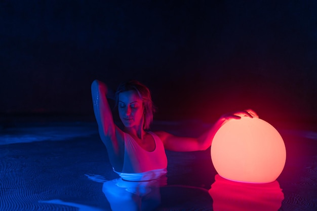 Mujer joven relajada en la piscina con luz de neón