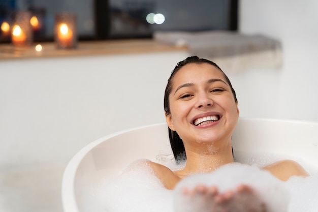 Mujer joven relajante y jugando con espuma mientras toma un baño