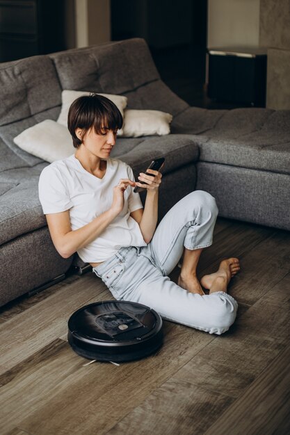 Mujer joven relajante mientras robot aspirador limpiando el piso