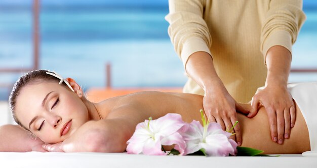 Mujer joven relajante en el salón de spa y recibiendo un masaje de cuerpo