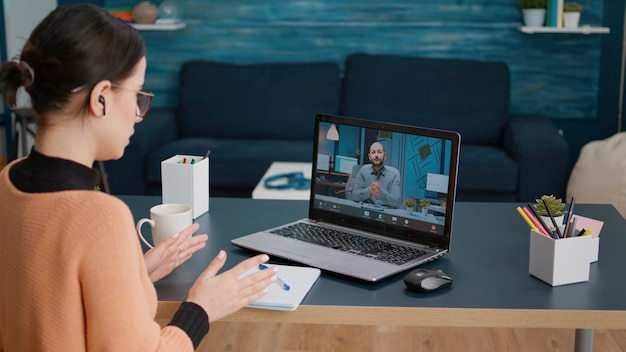 Mujer joven reunida con un maestro en una videollamada remota, hablando sobre la educación y la lección de la clase en línea. Estudiante charlando con un hombre en un seminario web de videoconferencia, usando una laptop con cámara web.