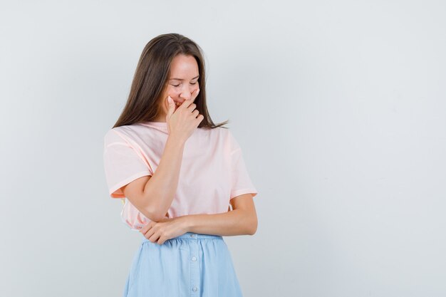 Mujer joven riendo con la mano sobre la boca en camiseta, falda, vista frontal.