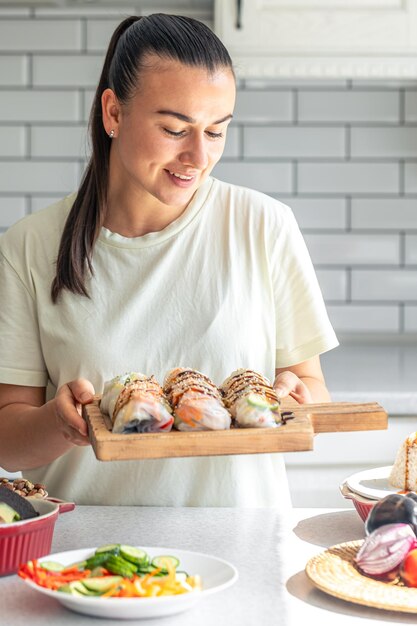 Foto gratuita una mujer joven con rollos de primavera en papel de arroz en la cocina