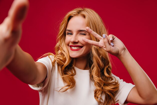 Mujer joven romántica con manicura de moda posando en la pared roja. Adorable dama rubia riendo