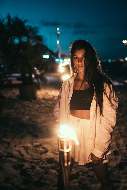 Mujer joven en ropa blanca con antorchas en la playa por la noche