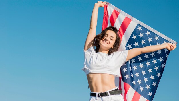 Mujer joven en ropa blanca con gran bandera de Estados Unidos