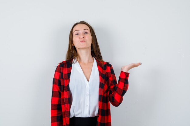 Mujer joven en ropa casual mostrando y mirando orgulloso, vista frontal.