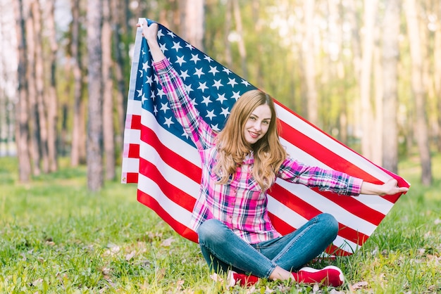 Mujer joven en ropa casual sentado en el suelo y sosteniendo la bandera estadounidense