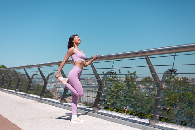 Mujer joven en ropa deportiva adecuada en el puente en la calurosa mañana soleada estirarse