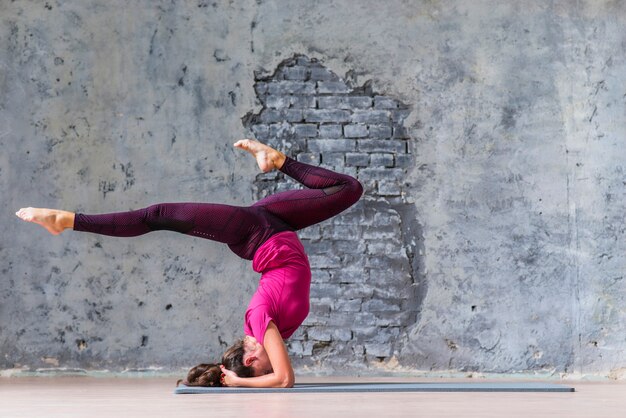 Mujer joven con ropa deportiva trabajando contra la pared gris