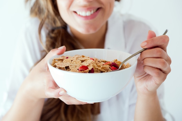 Mujer joven en ropa interior comiendo cereales. Aislado en blanco