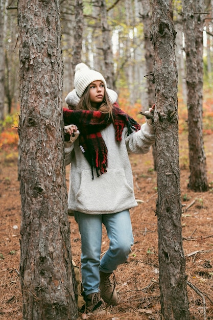 Foto gratuita mujer joven en ropa de invierno de pie junto a los árboles