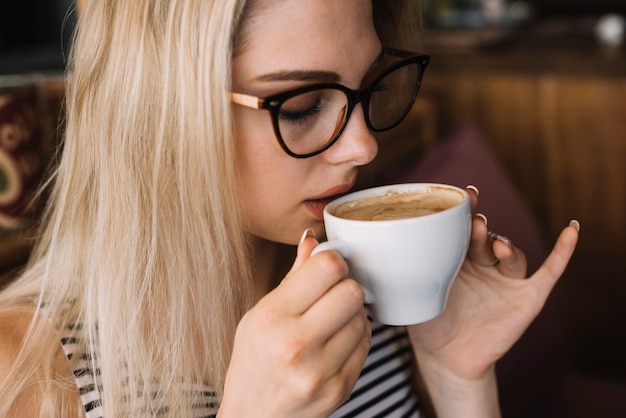 Mujer joven rubia con anteojos bebiendo café