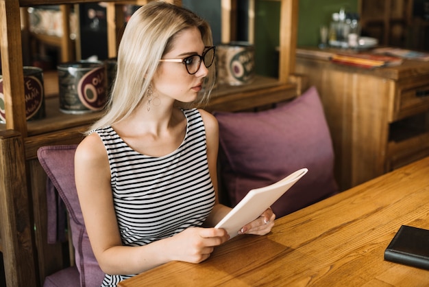 Mujer joven rubia con anteojos sosteniendo el menú en la mano en el restaurante