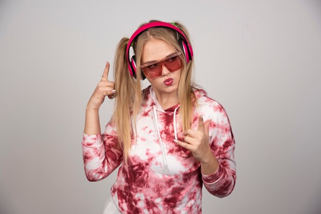 Mujer joven rubia en auriculares de color rosa apuntando a algún lugar.